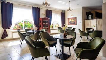 Un comedor con mesas redondas y sillas verdes, una araña y vistas a un jardín a través de grandes ventanales.