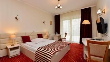 A hotel room with a large bed, a desk, a chair, a TV, and a window with curtains.