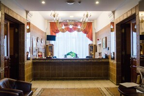 A reception area with a reception desk, a chandelier, and a large window with curtains.