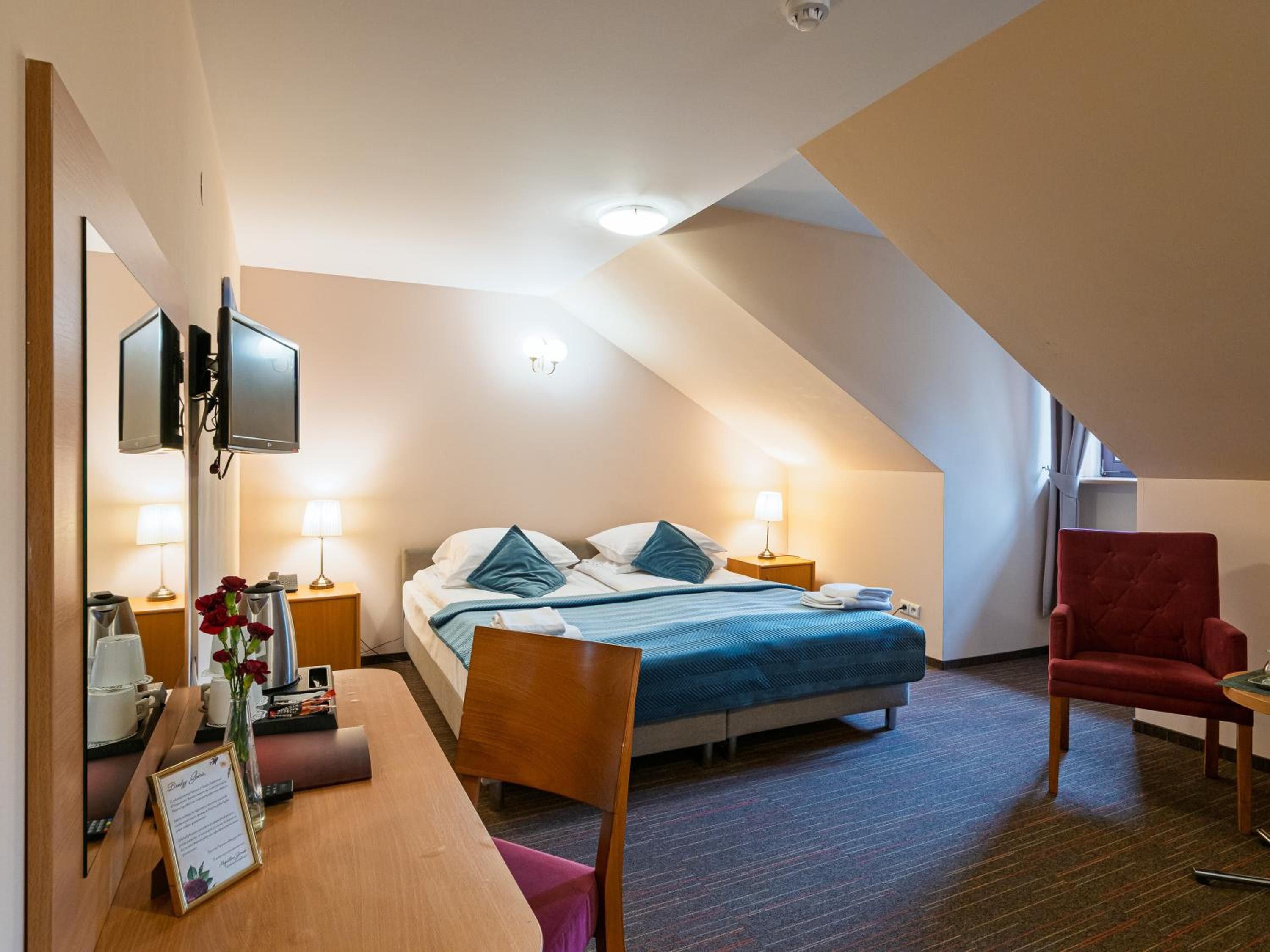 A hotel room with a bed, bedside tables, a desk, a chair, and a TV.