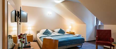 A hotel room with a bed, bedside tables, a desk, a chair, and a TV.