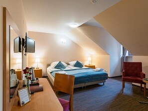 A hotel room with a bed, bedside tables, a desk, a chair, and a TV.