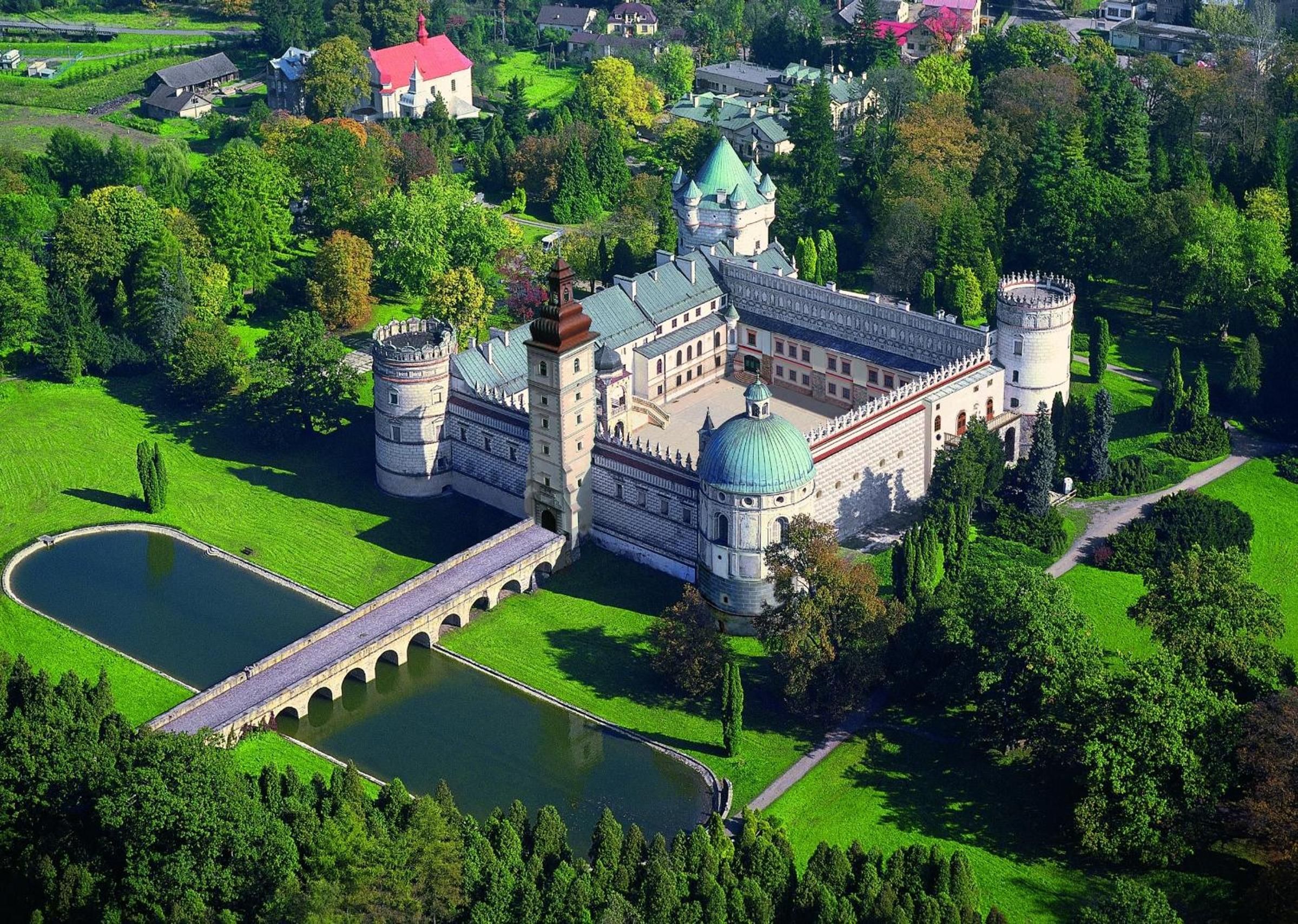 A castle with a moat, a bridge, and a large green lawn.