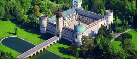 A castle with a moat, a bridge, and a large green lawn.