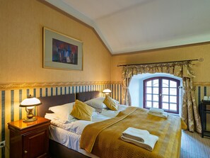 A hotel room with a large bed, two bedside lamps, a painting on the wall, and a window with curtains.