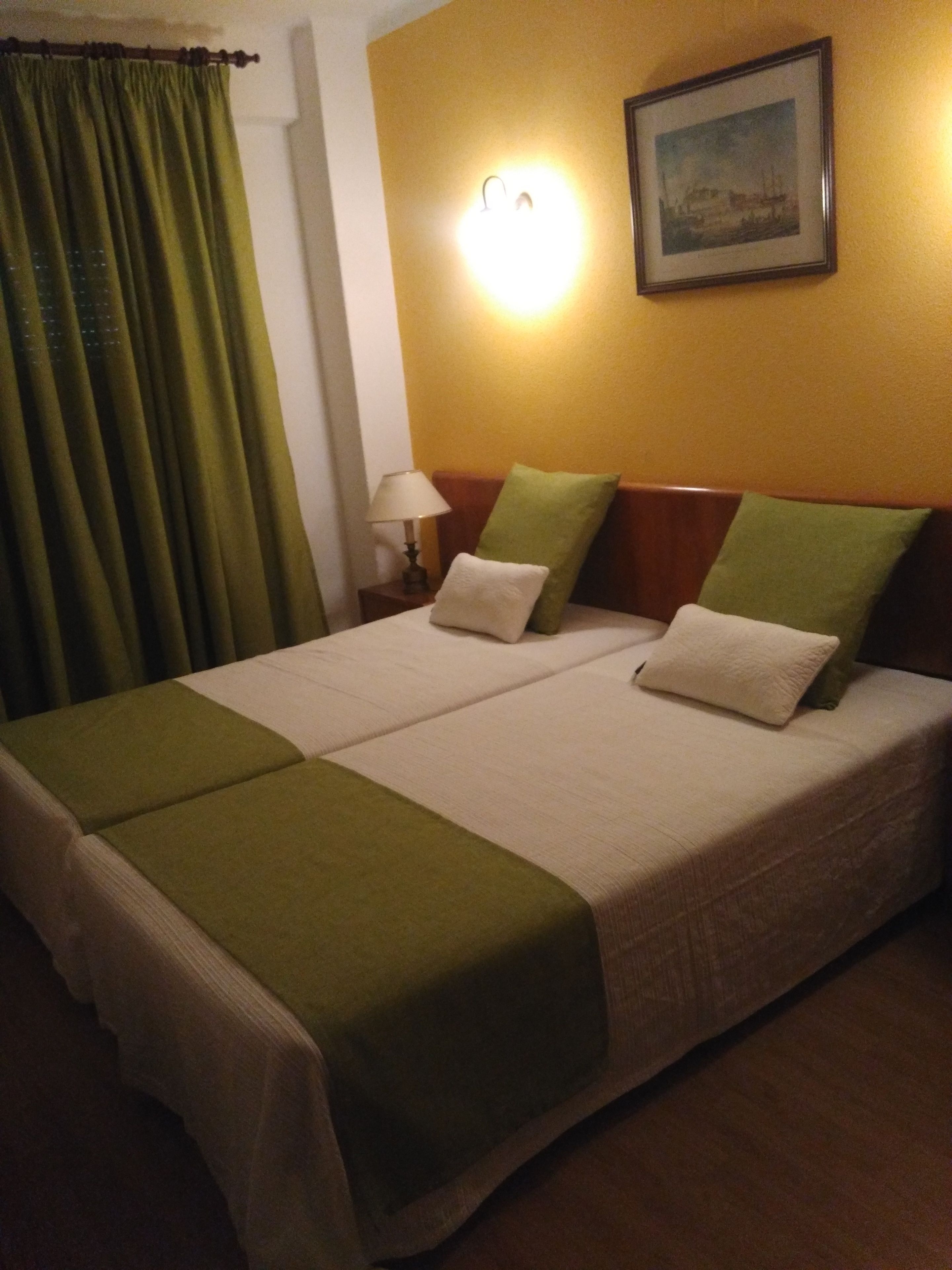 Een tweepersoonsbed met twee kussens, een bedlampje en een lijst met een afbeelding aan de muur.