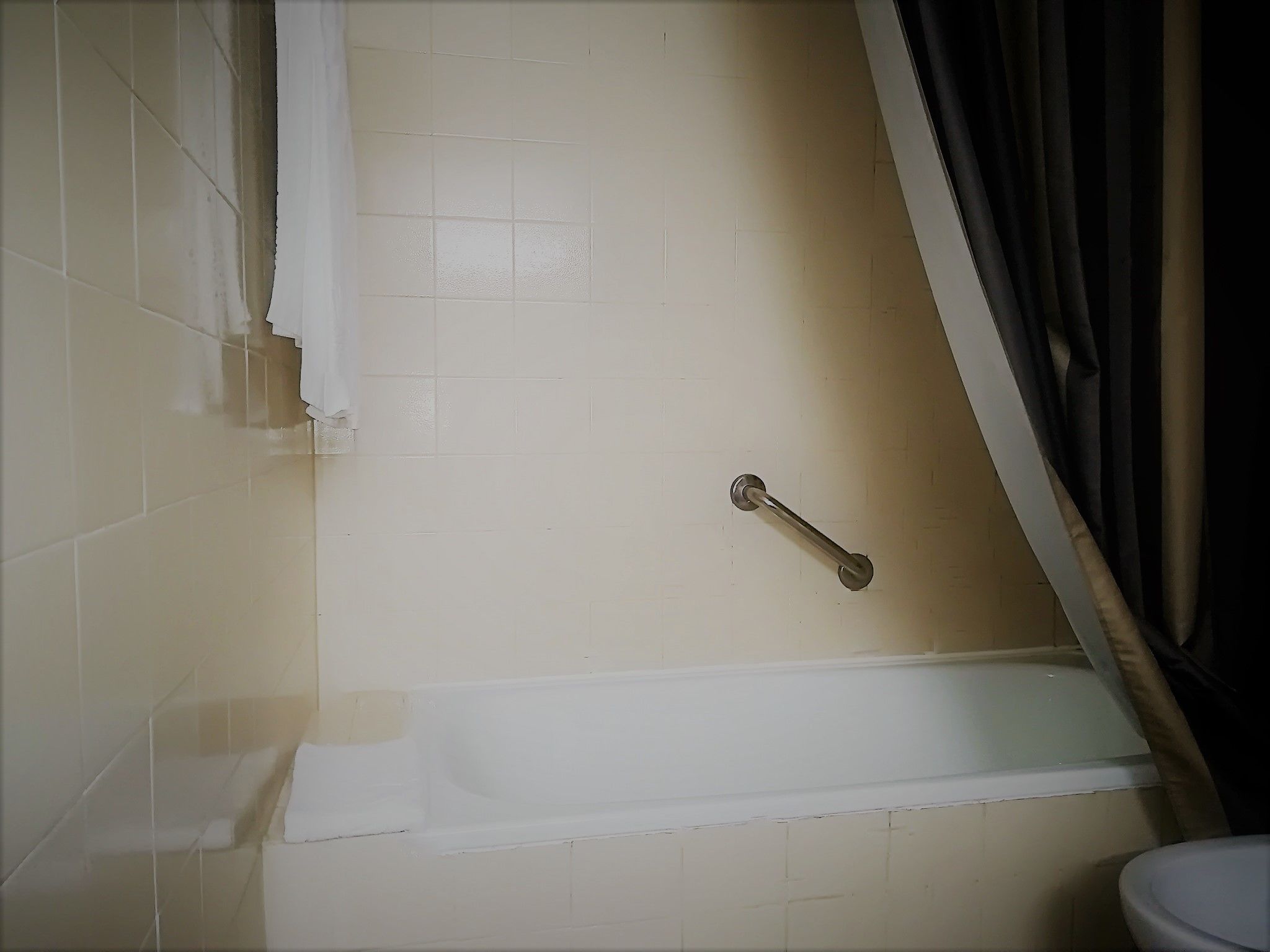 A bathroom with a bathtub, a handrail, and a toilet.
