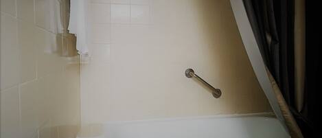 A bathroom with a bathtub, a handrail, and a toilet.