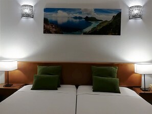 A hotel room with a large bed, two green pillows, a wooden headboard, two wall sconces, and a framed landscape painting above the bed. - Apartamentos Lindomar (Silves)