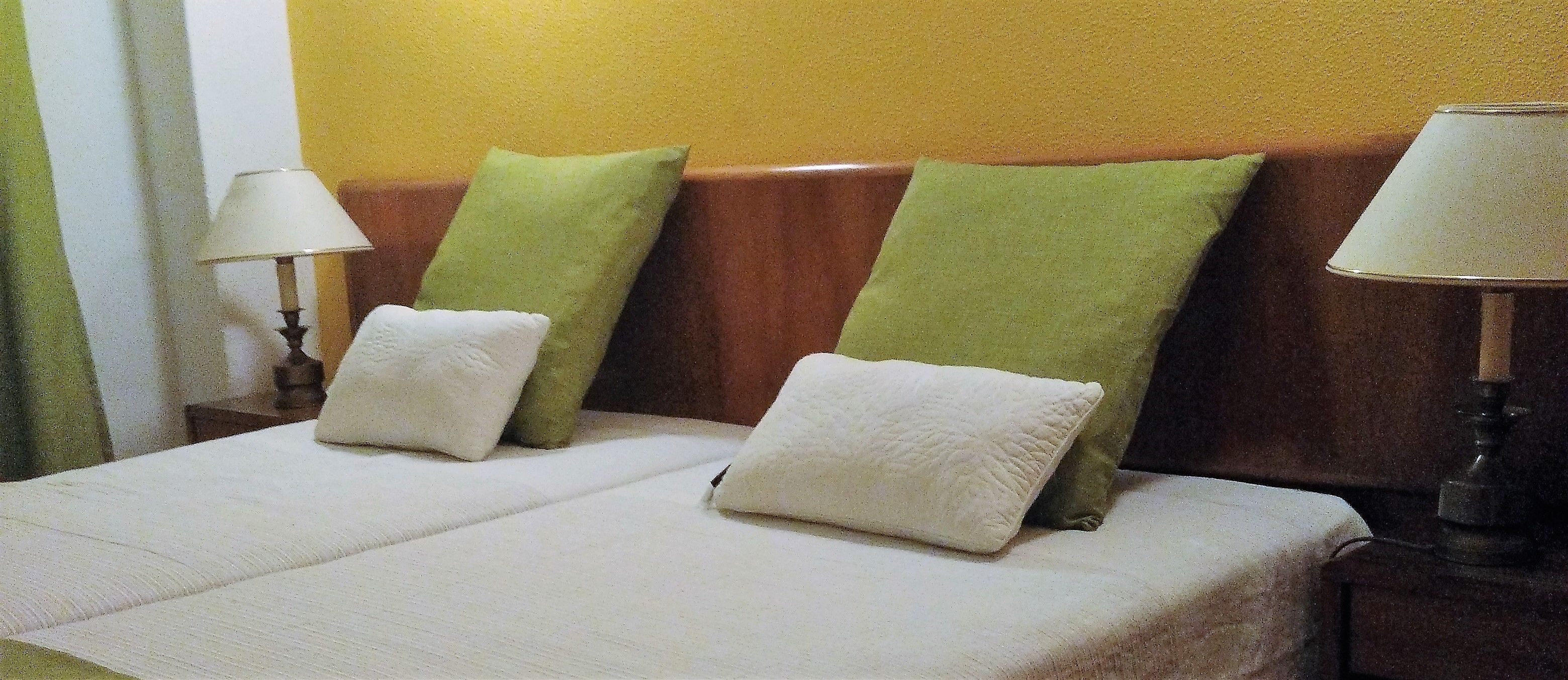 Un letto con due cuscini, una testiera in legno e due abat-jour.