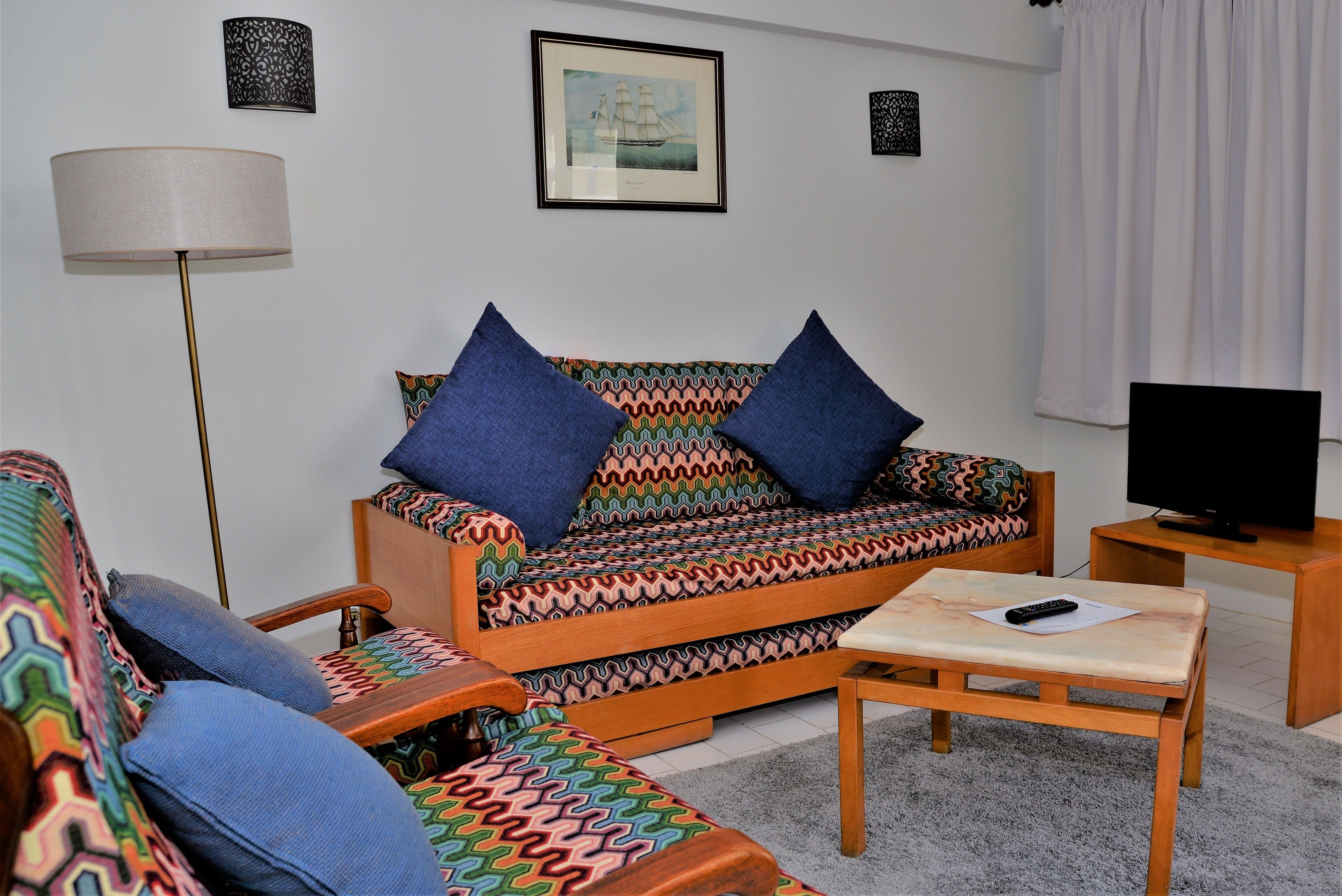 Ein Wohnzimmer mit Sofa, Sessel und einem kleinen Tisch mit Fernbedienung.
