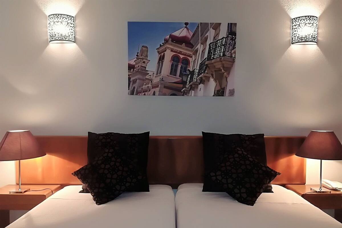 A hotel room with a bed, two nightstands, two lamps, and a wall-mounted picture of a building.
