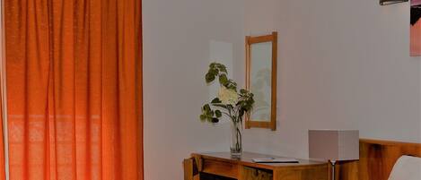 A hotel room with a wooden desk, a mirror, a lamp, and a bed.