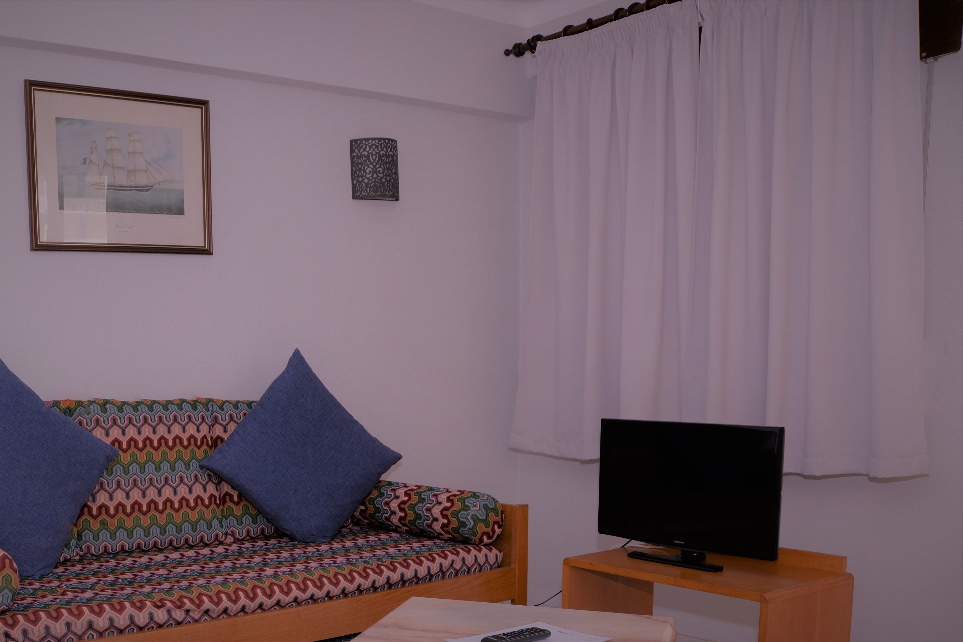 A living room with a patterned sofa, a television on a wooden stand, and a framed picture on the wall.