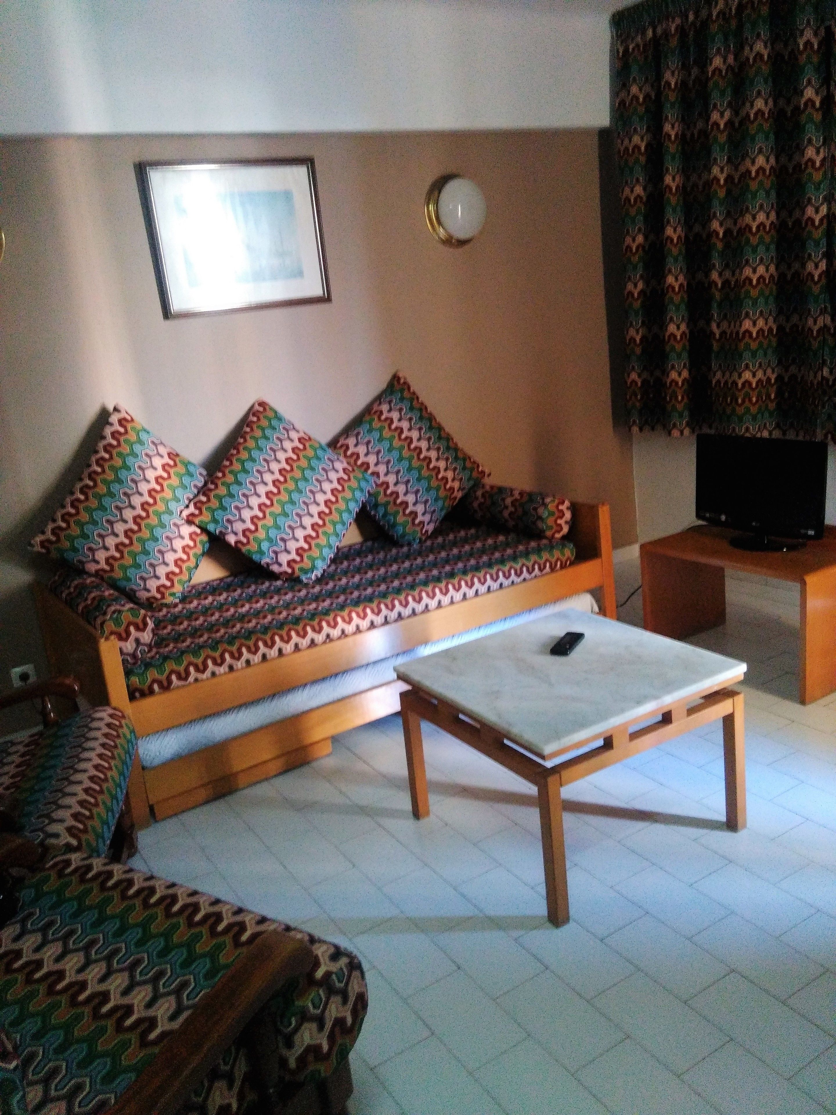 Un salon avec un canapé, des coussins à motifs, un téléviseur posé sur un meuble et une table basse.