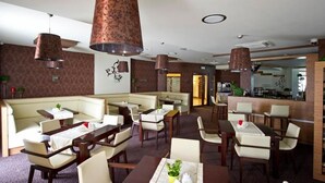 Un espace de restauration d’hôtel avec des banquettes et des tables, un bar et une vue sur la cuisine.