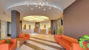 Un hall d’hôtel avec un comptoir d’accueil, des sièges orange et un lustre moderne.