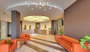 A hotel lobby with a reception desk, orange seating, and a modern chandelier.