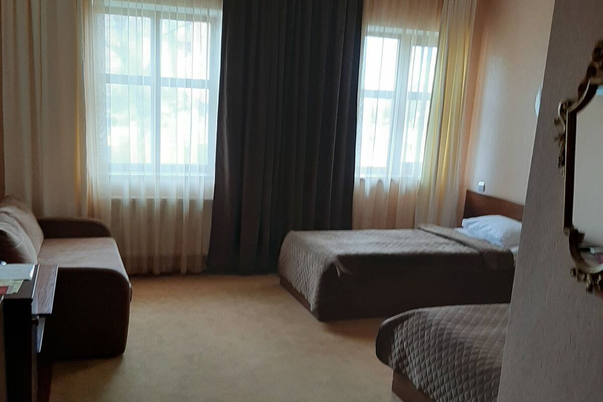 A hotel room with two beds, a desk, and a large window with curtains.