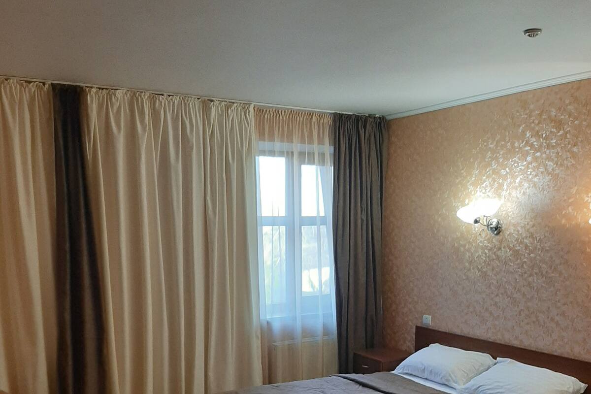 A hotel room with two beds, a window with curtains, a wall-mounted light fixture, and a carpeted floor.