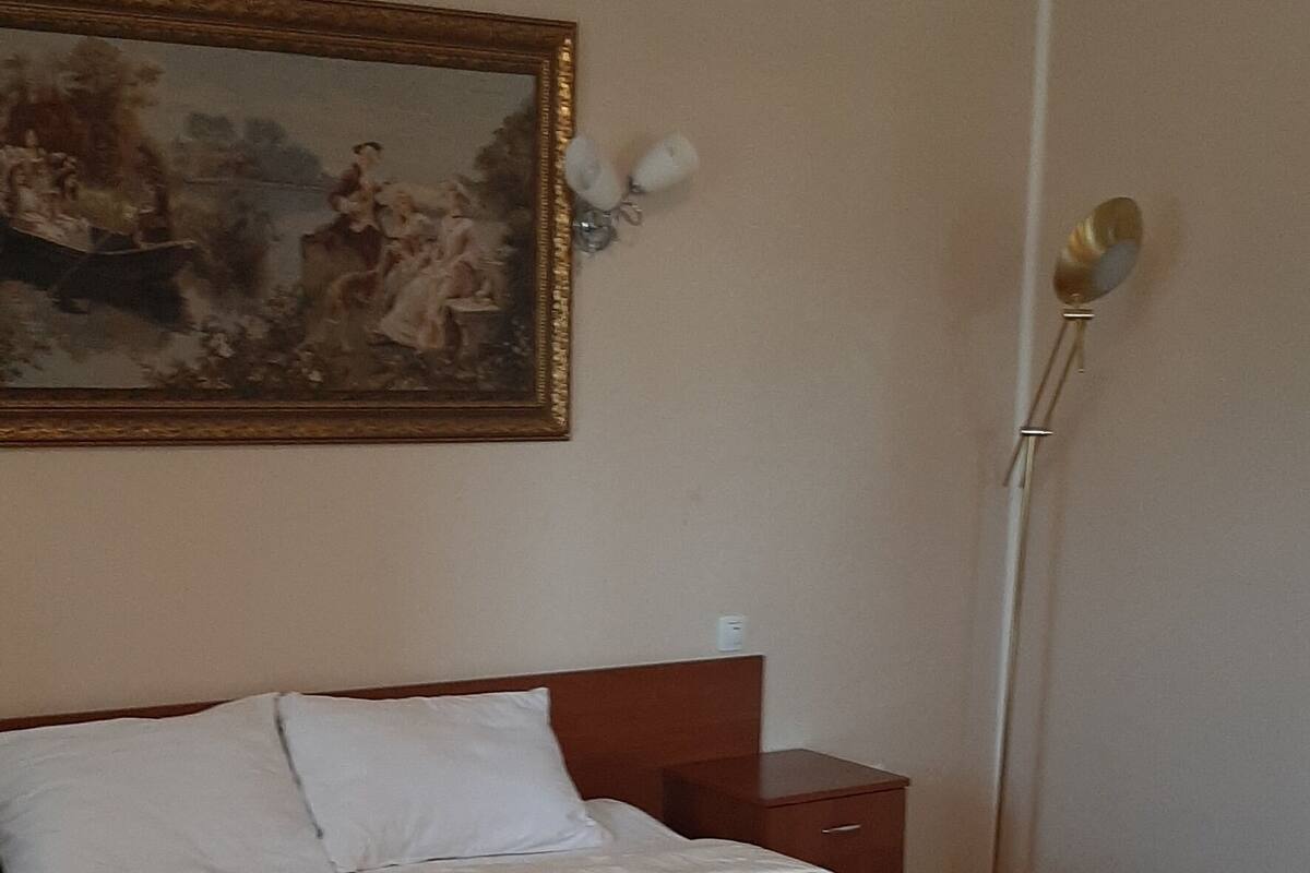 A bedroom with a large bed, a nightstand, a lamp, and a painting on the wall.
