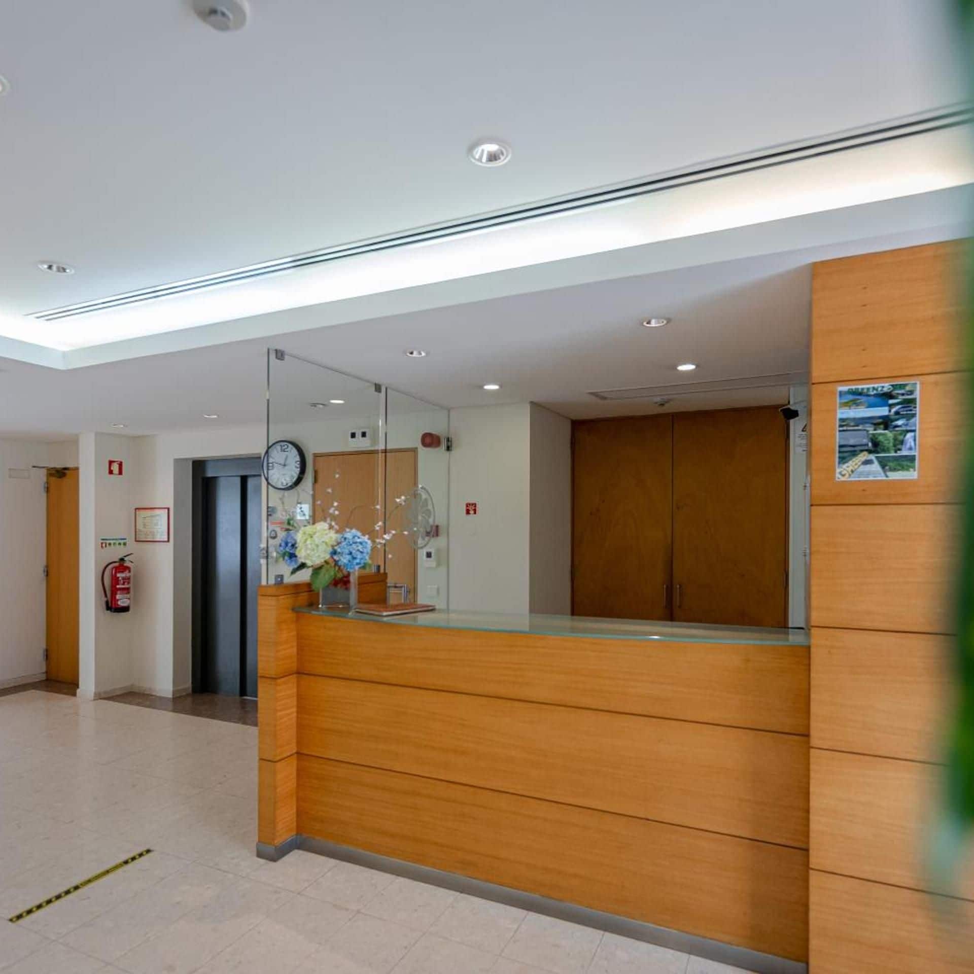 A reception area with a wooden reception desk, a clock, and a fire extinguisher on the wall.