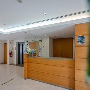 Una zona d'entrada amb un taulell de recepció de fusta, un rellotge i un extintor fixat a la paret.