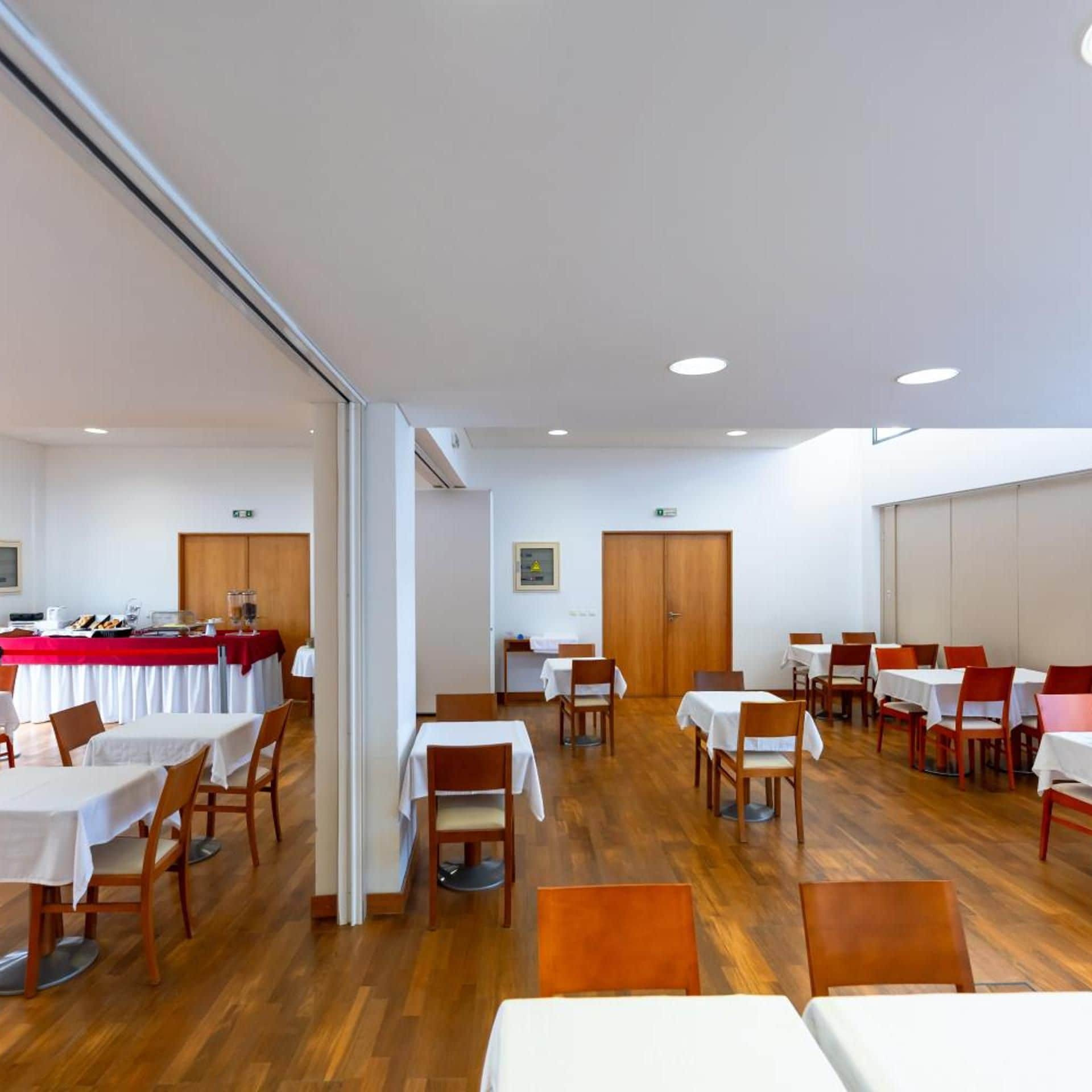 A dining area with tables and chairs, a buffet setup, and a wooden floor.