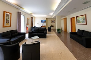 Un vestíbul d'hotel amb sofàs negres, un televisor de pantalla plana i obres d'art a les parets.