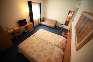 A hotel room with a bed, a desk, a chair, a sofa, a lamp, a mirror, and a painting on the wall. - Matriz (Ponta Delgada)