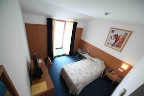 A hotel room with a bed, a desk, a chair, a window with curtains, a painting on the wall, and a door. - Matriz (Ponta Delgada)