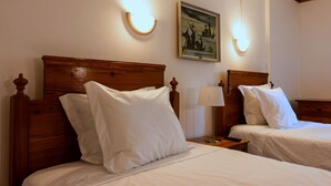 Two wooden beds with white linens and headboards, a nightstand with a lamp, and a framed painting on the wall. - Casa Do Jardim (Ponta Delgada)