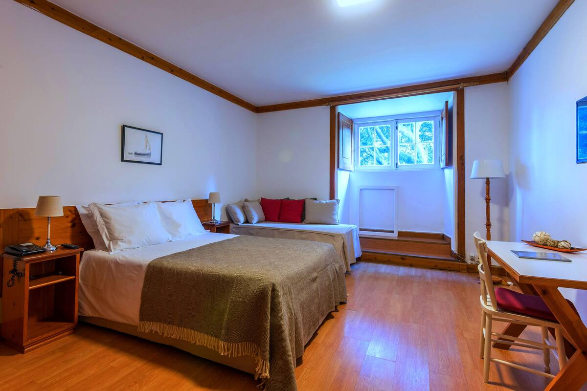A bedroom with a bed, bedside table, lamp, and a window with a view.