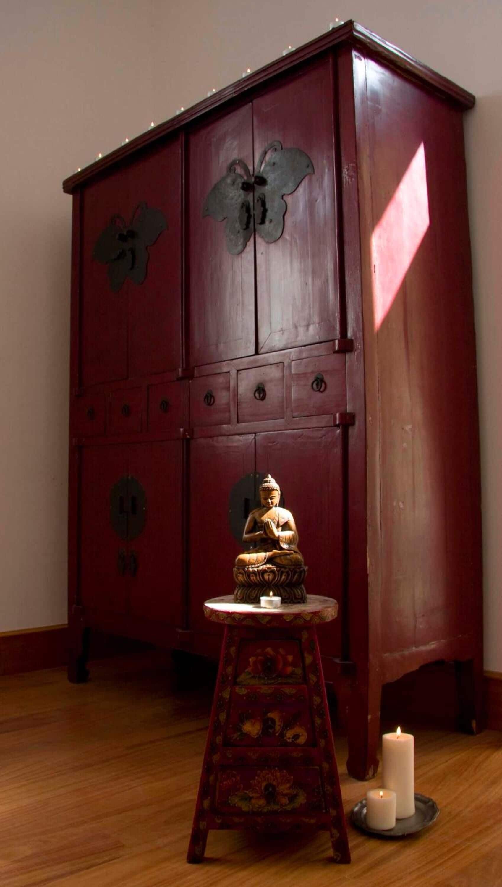 Et træskab med blomstermotiver og en Buddha-figur på et lille bord.