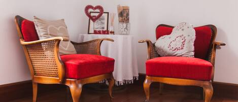 Two red upholstered chairs with wooden frames, a small table with a white tablecloth, and a wall with a heart-shaped decoration and a framed picture.