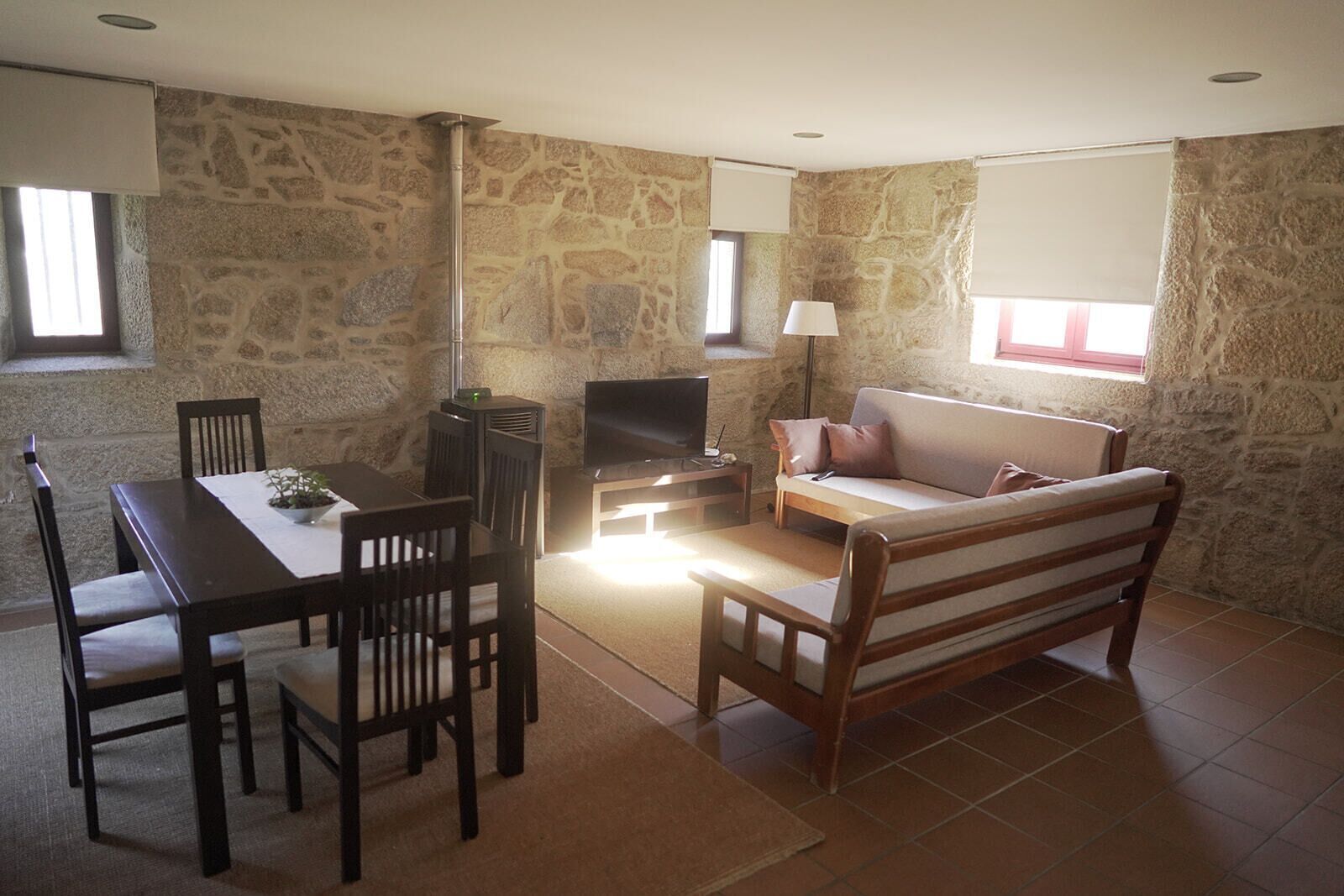 A room with stone walls, a sofa, a TV, a dining table with chairs, and a lamp.