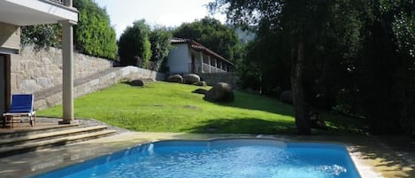 A swimming pool with a stone wall and a grassy area.