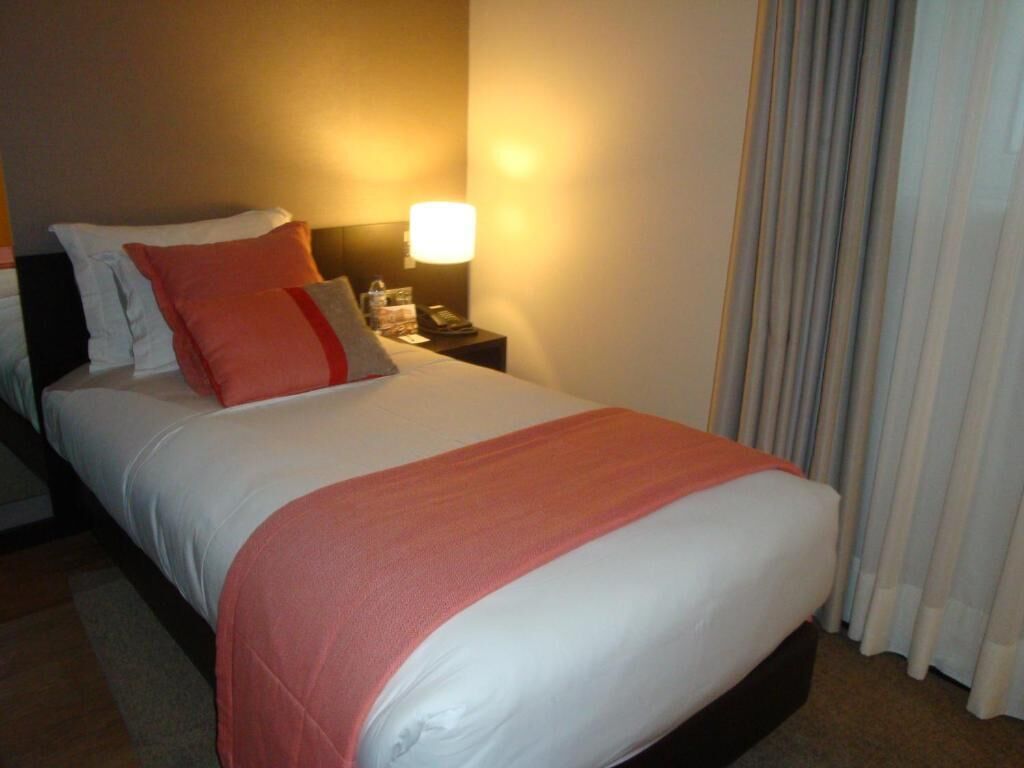 A hotel room with a bed, a nightstand with a lamp, and a window with curtains.