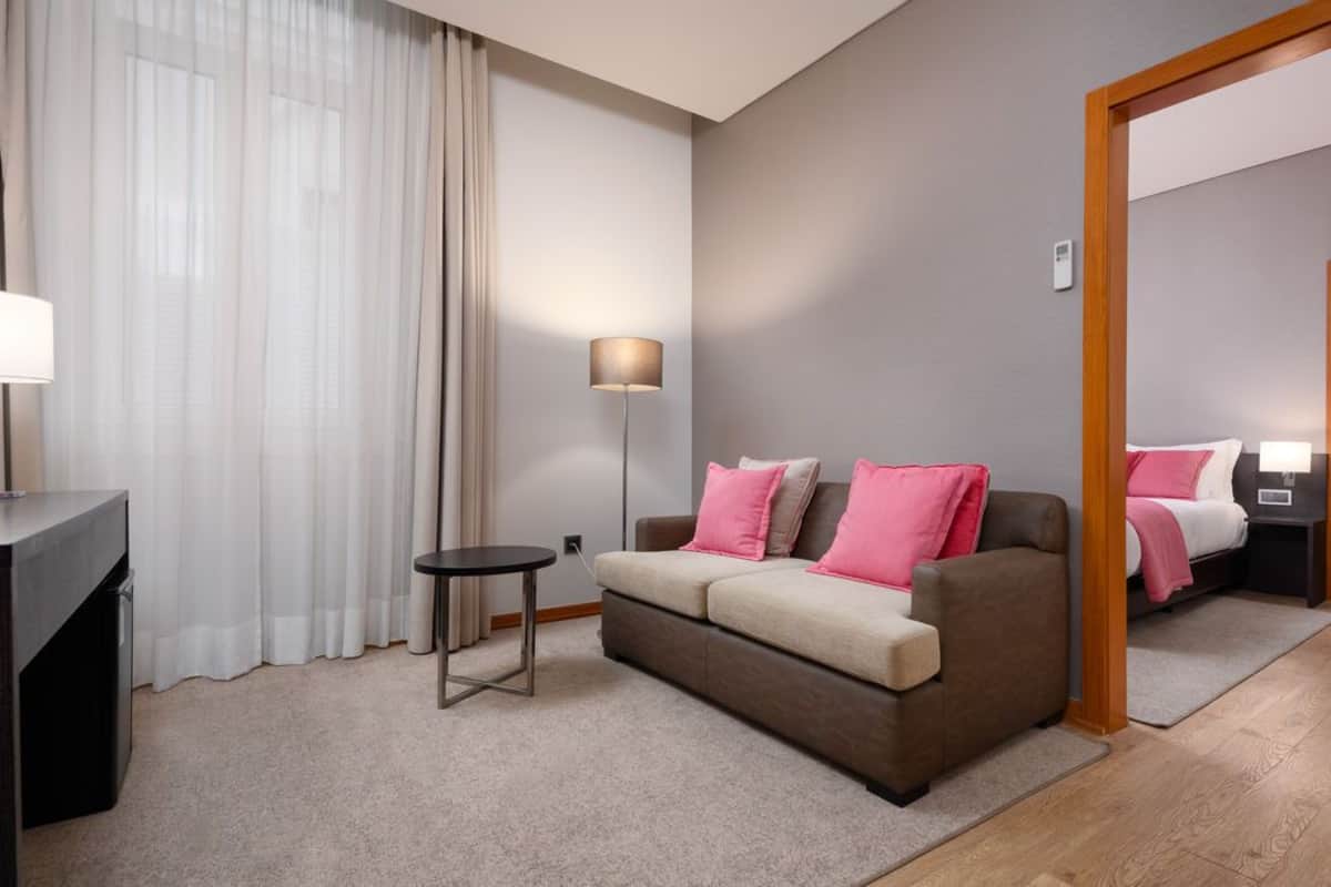 Ein modernes Hotelzimmer mit Sofa, einem kleinen Tisch, einer Lampe und einem Bett mit Nachtisch.
