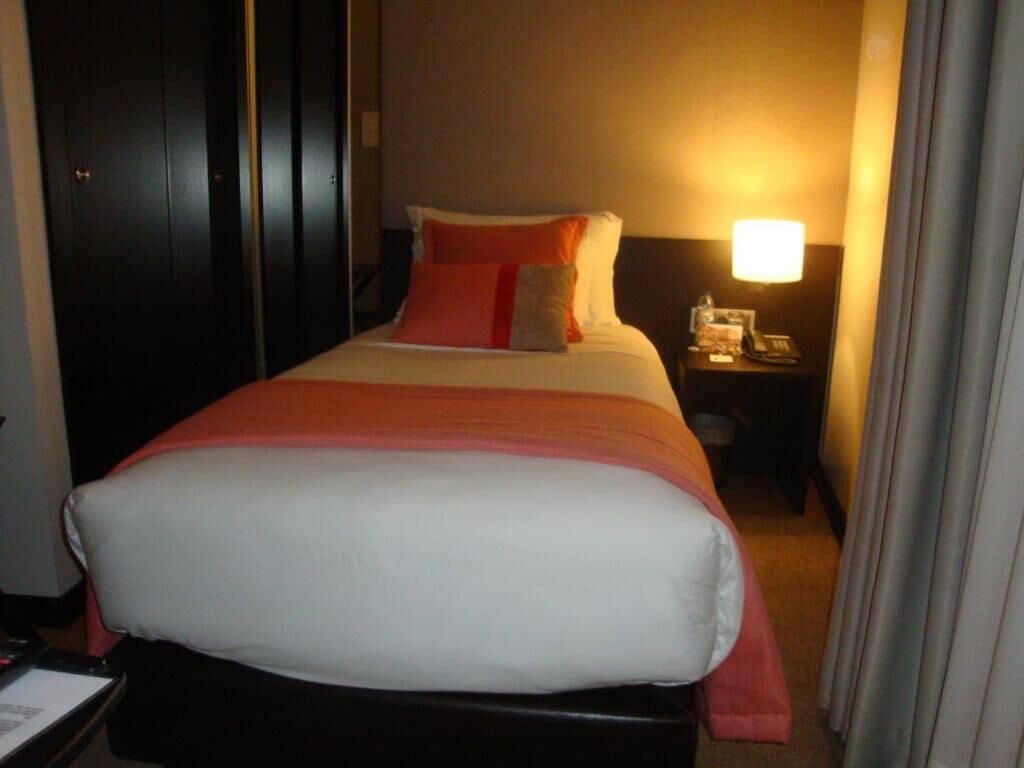 A hotel room with a bed, a nightstand with a lamp, and a door.