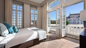Een slaapkamer met een groot bed, een balkon met uitzicht op gebouwen en een raam met gordijnen.