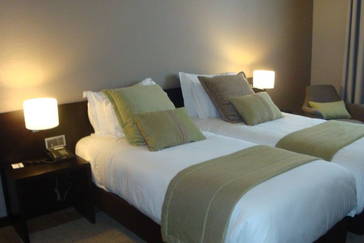 Ein Hotelzimmer mit zwei Betten, jeweils mit weißer Bettwäsche und grünen Zierkissen. An den Nachttischen stehen Lampen und ein Telefon.