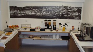 A breakfast bar with various food items, a coffee station, and a large black and white cityscape painting on the wall. - Botânico (Coimbra)