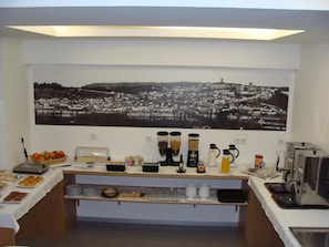 A breakfast bar with various food items, a coffee station, and a large black and white cityscape painting on the wall. - Botânico (Coimbra)