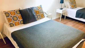 A neatly arranged bedroom with a large bed, a bedside table with a lamp, and a small table with a phone. - Botânico (Coimbra)