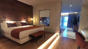 A modern hotel room with a large bed, bedside tables, a bench, a mirror, and a view into the adjacent living area. -  Alambique Hotel Resort & Spa  (Fundao)