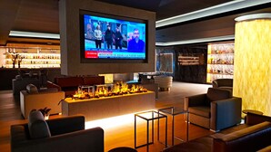 A modern lobby with comfortable seating, a large TV screen displaying a news program, and a fireplace. -  Alambique Hotel Resort & Spa  (Fundao)