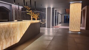 A modern reception area with a marble counter, a vase of autumn leaves, and a polished floor. -  Alambique Hotel Resort & Spa  (Fundao)