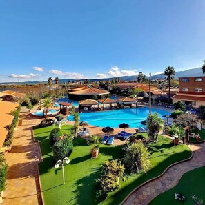 A resort with a large swimming pool, sun loungers, and a well-maintained garden.