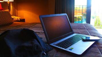Una laptop sobre una cama, con una manta, un almohadón y una lámpara al fondo.